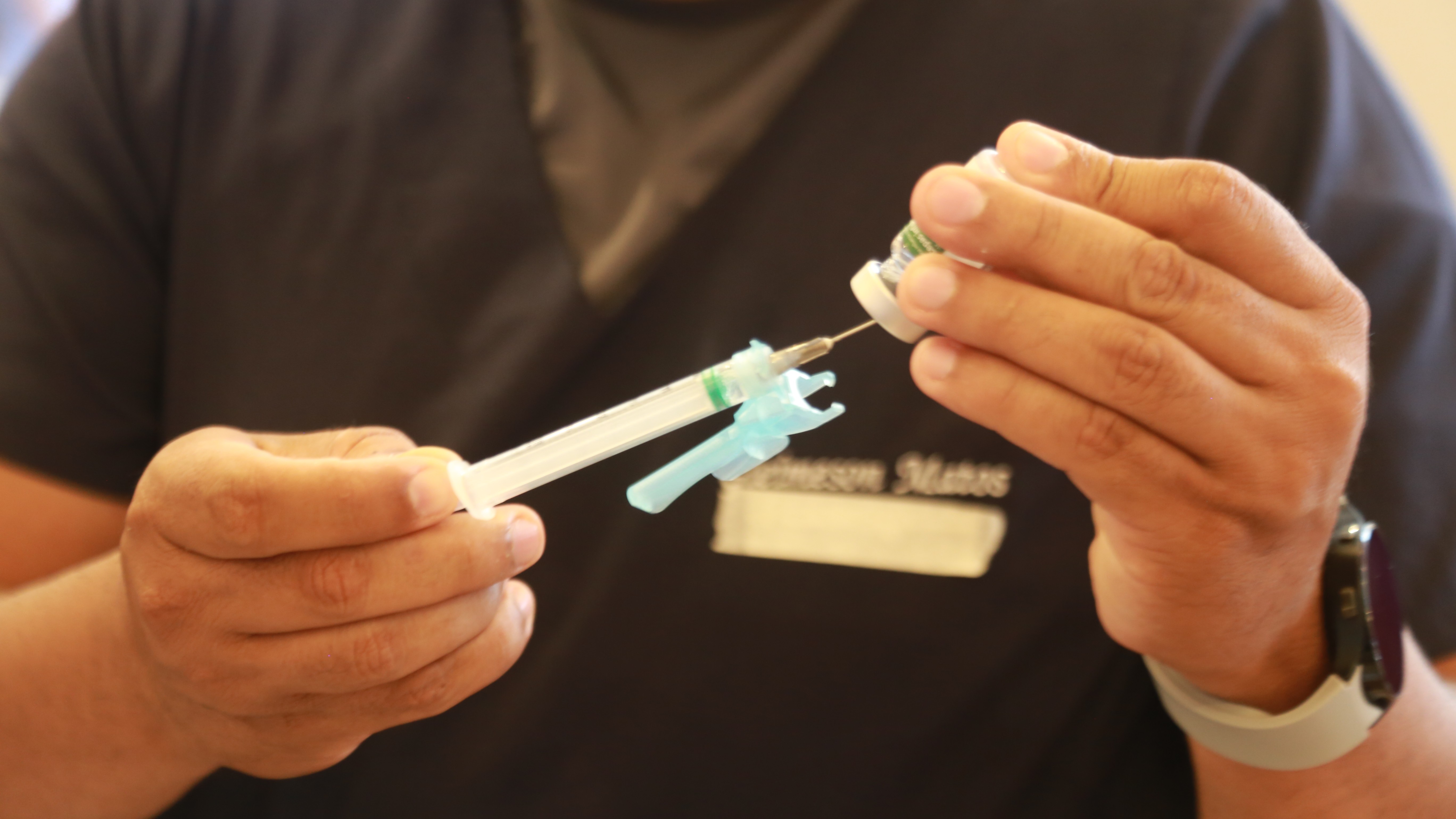 a foto mostra as mãos de um enfermeiro preparando uma dose de vacina